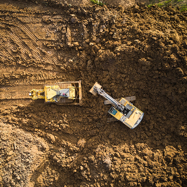 Bulldozer is scraping a layer of soil and excavator is digging and dumping dirt