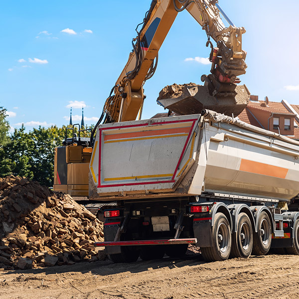 Heavy excavatore machine uploading waste and debris rubble into dump truck at construction site. Building dismantling and construction waste disposal service. Construction site industrial background.