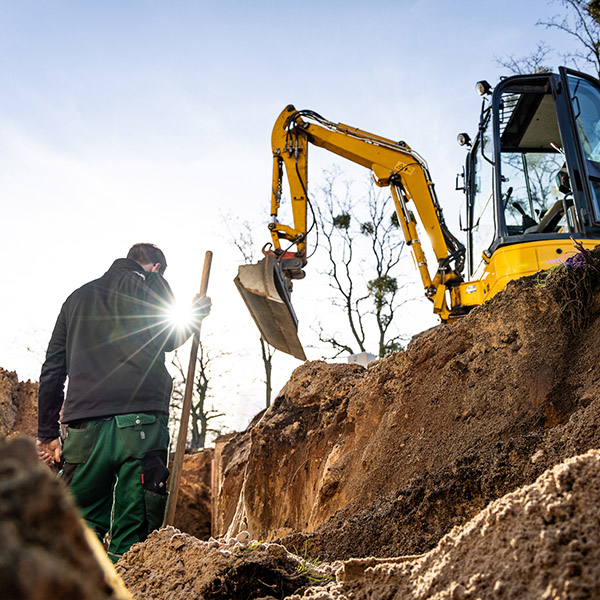 Excavation and earthwork in progress at a construction site, featuring an operator and excavator machinery. Shot from inside the hole in the ground.
