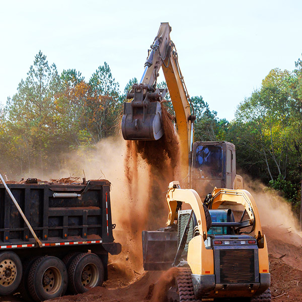 Heavy machinery moves soil, debris on construction site surrounded by trees during fall season.